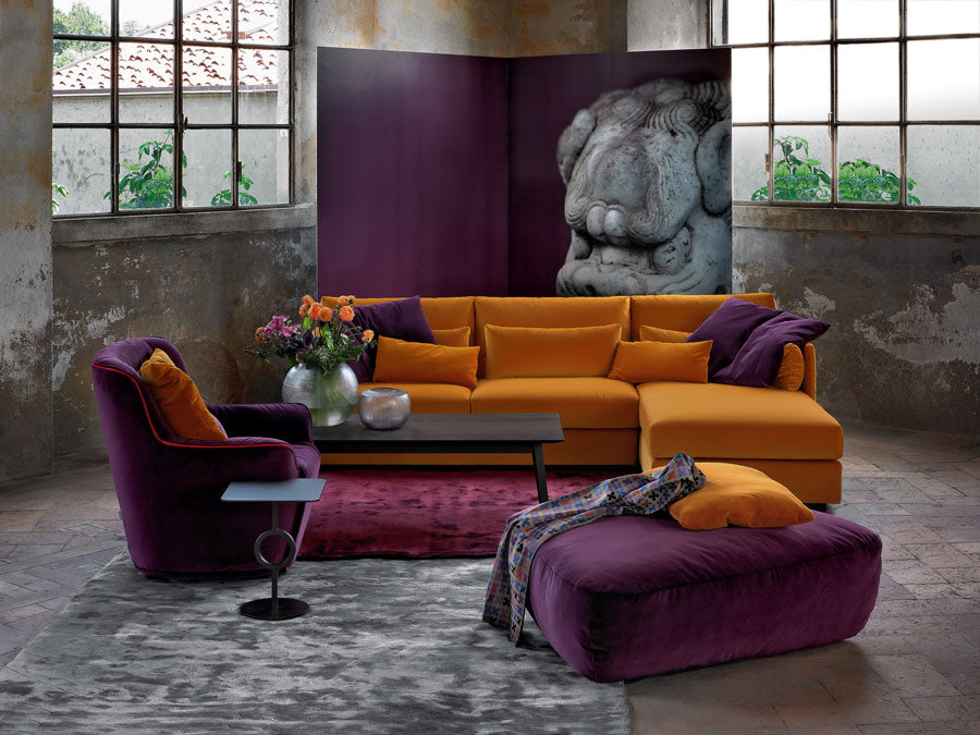 Industrial loft interior with orange sectional sofa, purple armchair, ottoman, and stone sculpture