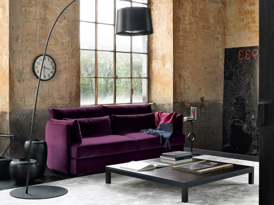 Industrial living room view with purple velvet sofa, black coffee table, arc lamp