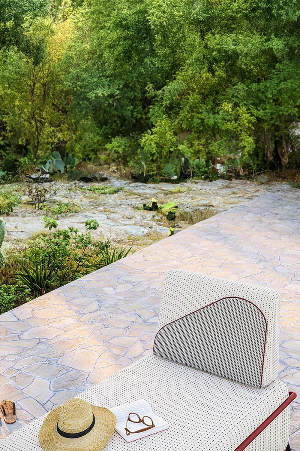 Outdoor chaise lounge on stone patio overlooking lush greenery