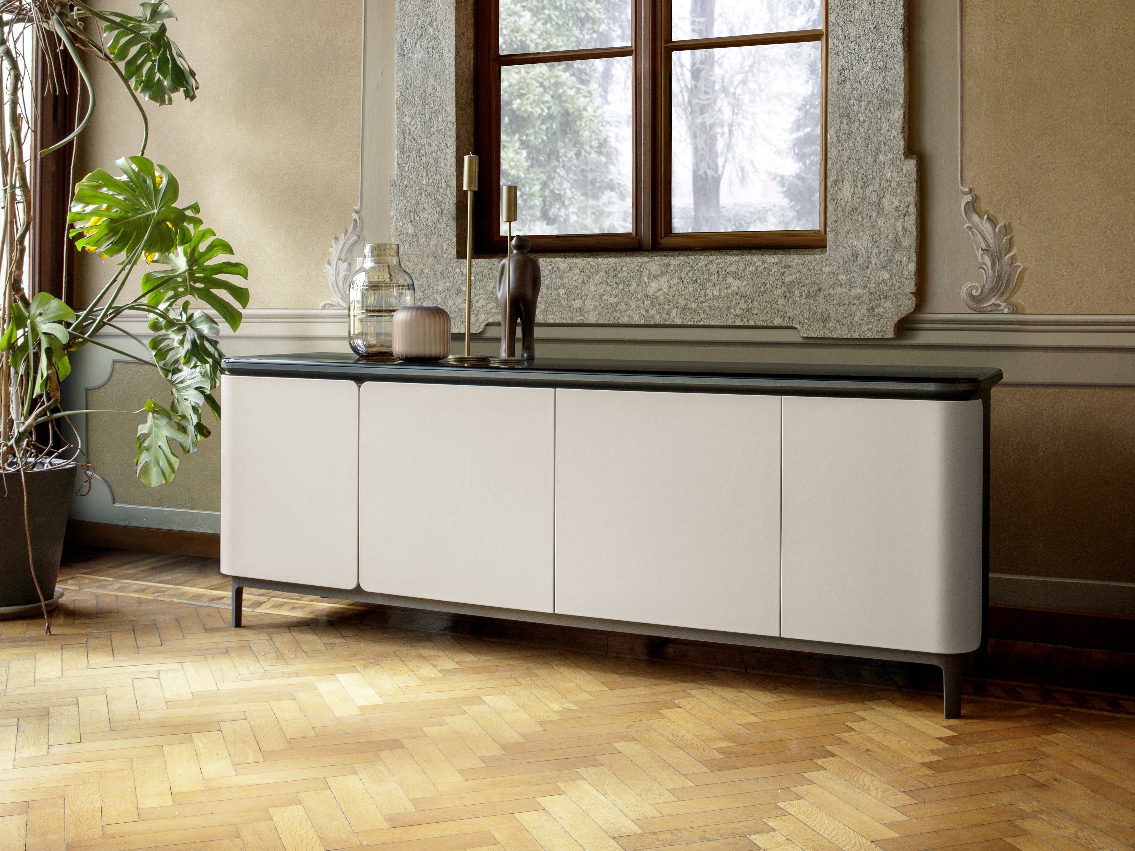 Modern sideboard cabinet in historic room with monstera plant and window.