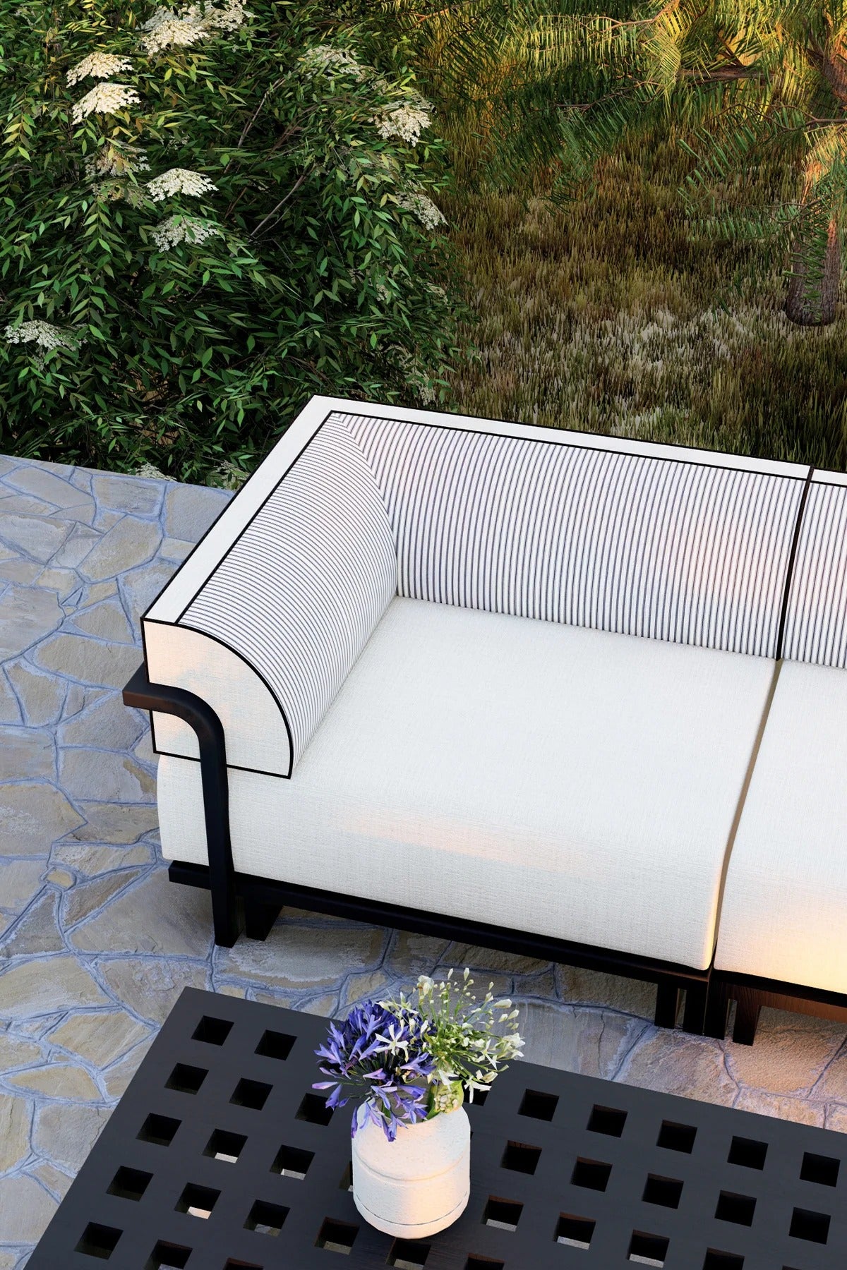 White outdoor sofa with black frame on a stone patio, surrounded by greenery.