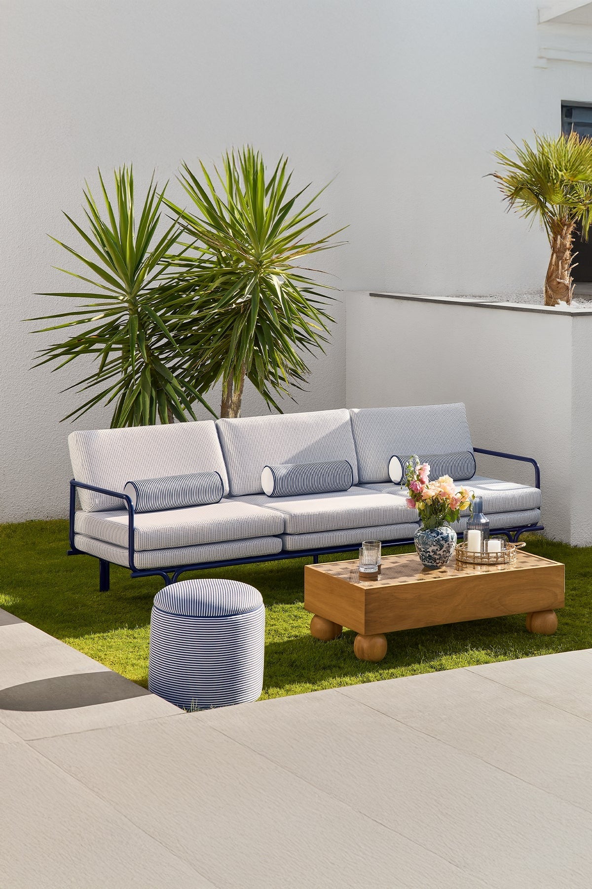 Outdoor sofa, wood coffee table, striped ottoman on green grass