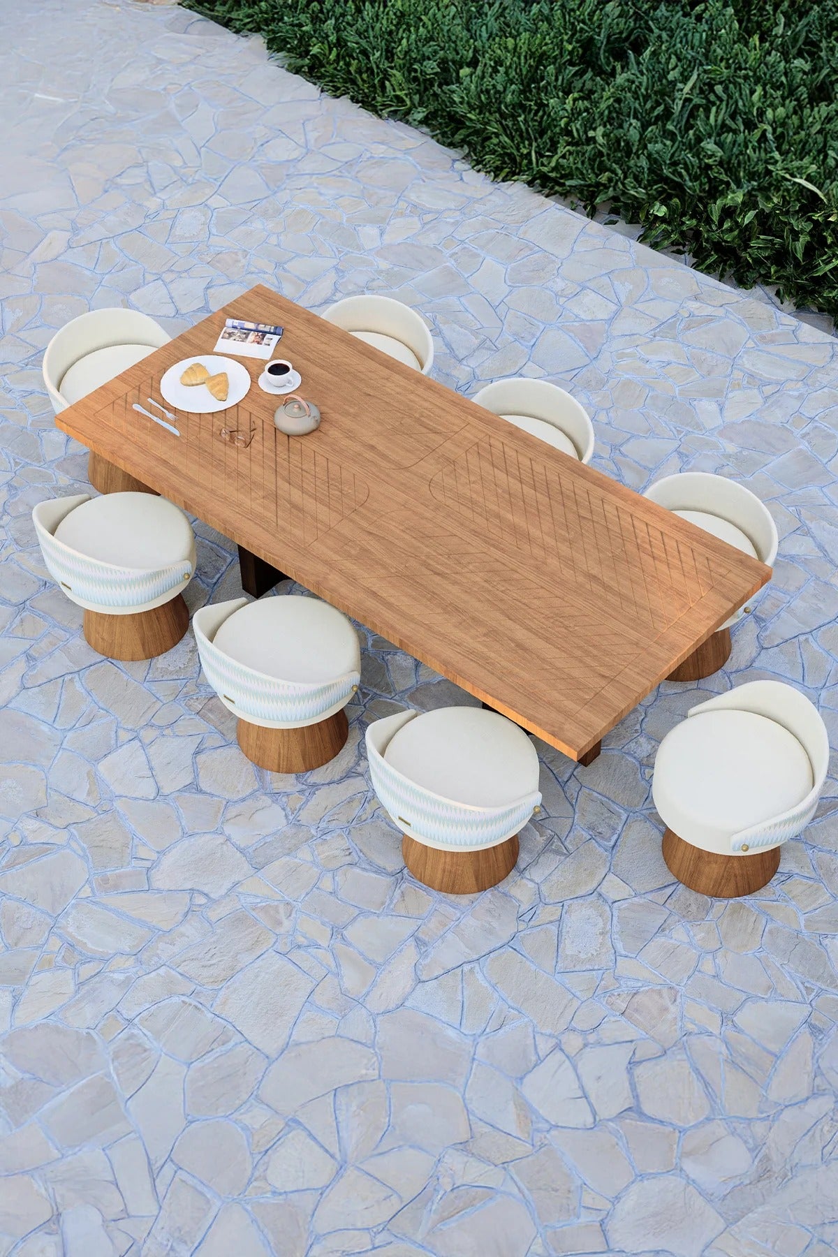 Modern outdoor dining area featuring iroko wood table and curved-back chairs on a stone patio with garden backdrop