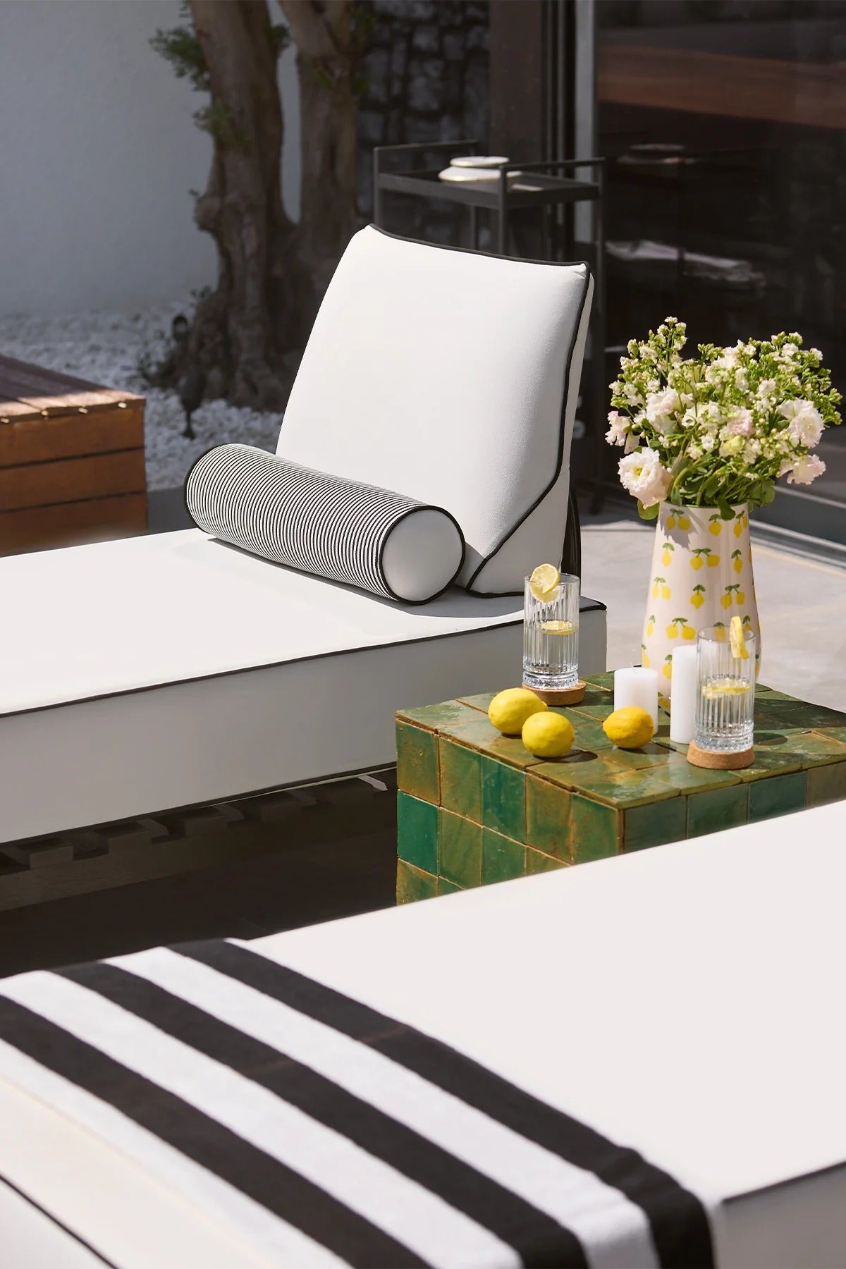 Outdoor seating area with a white cushioned chair, striped cover, and small table with lemons and a vase.