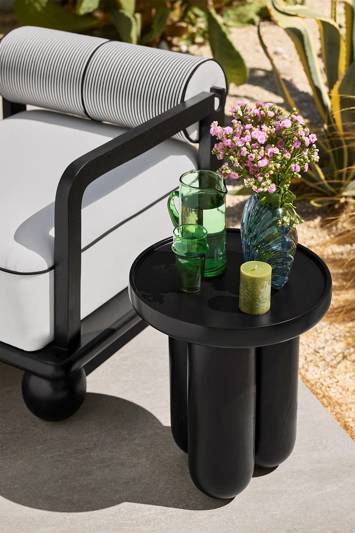 Black side table with decorative items next to a modern armchair outdoors.
