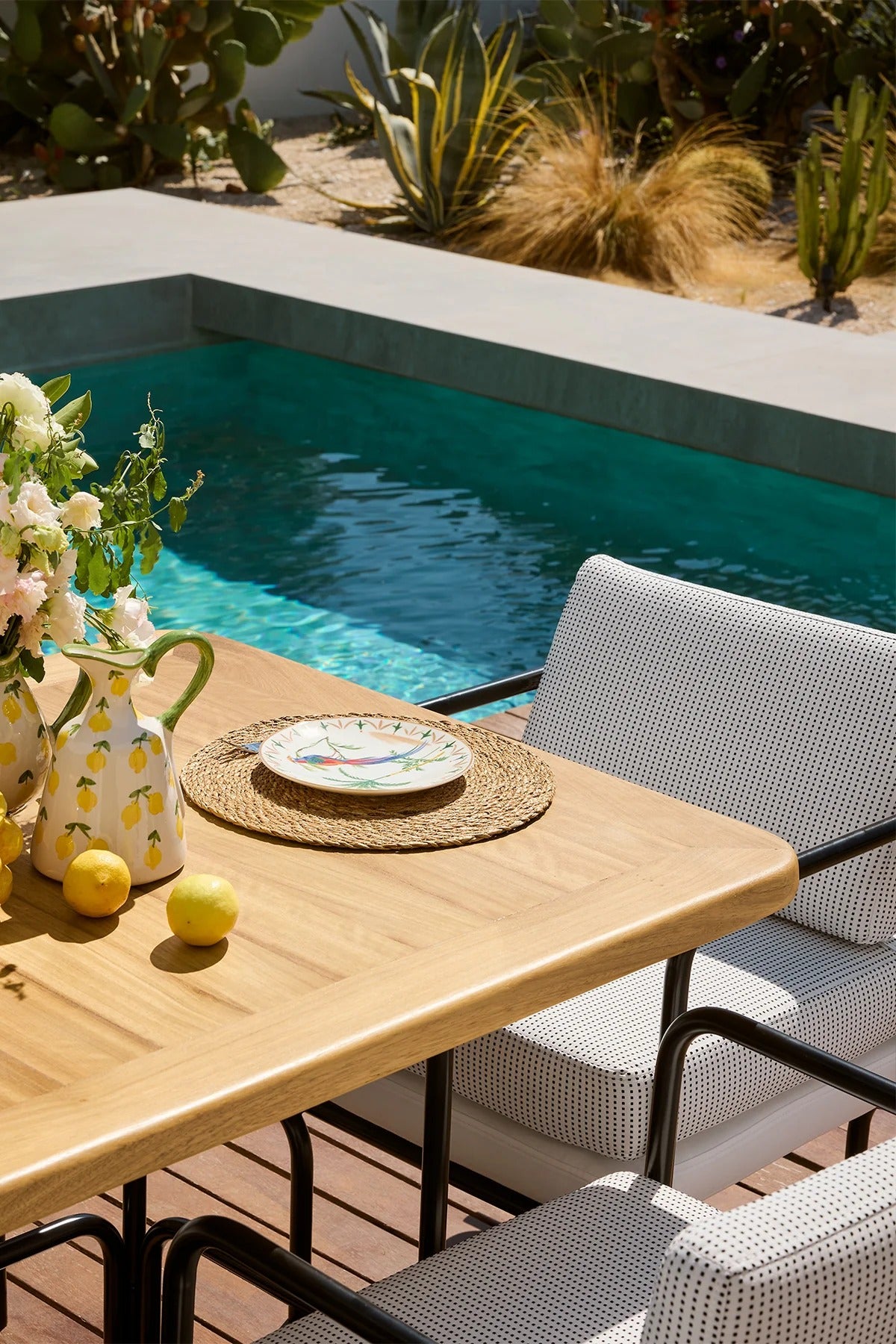 Outdoor setting with a table by a pool, featuring a teapot and lemons.