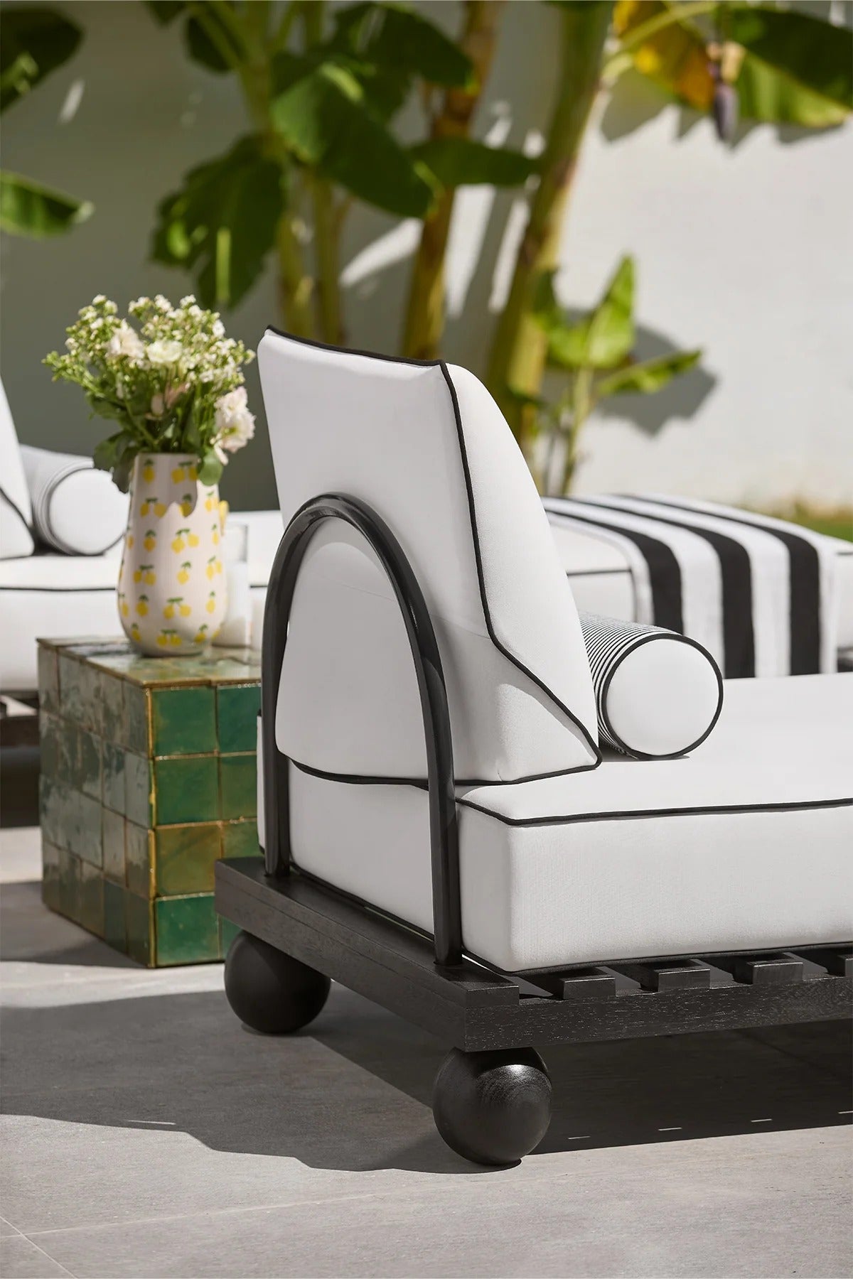 White outdoor chair with black accents on a patio with plants and a table in the background