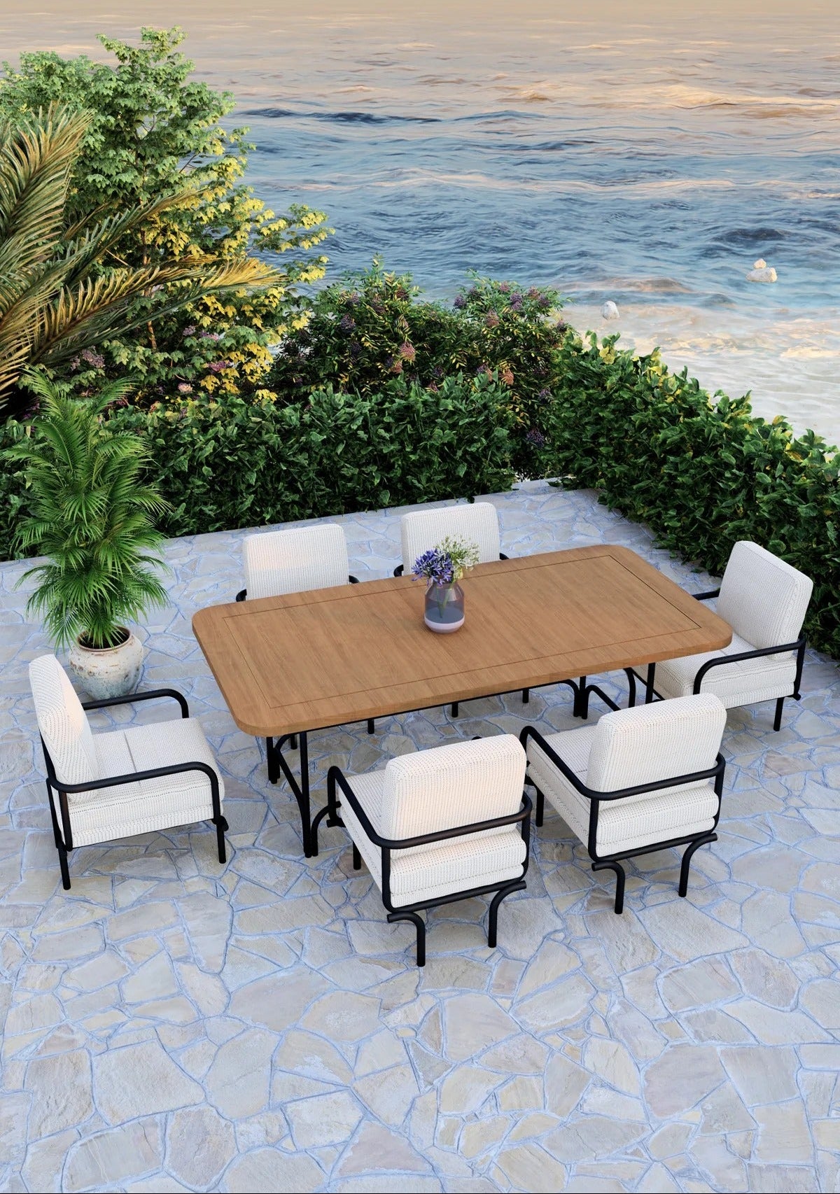 Outdoor patio set with a wooden table and chairs on a stone patio by the ocean.