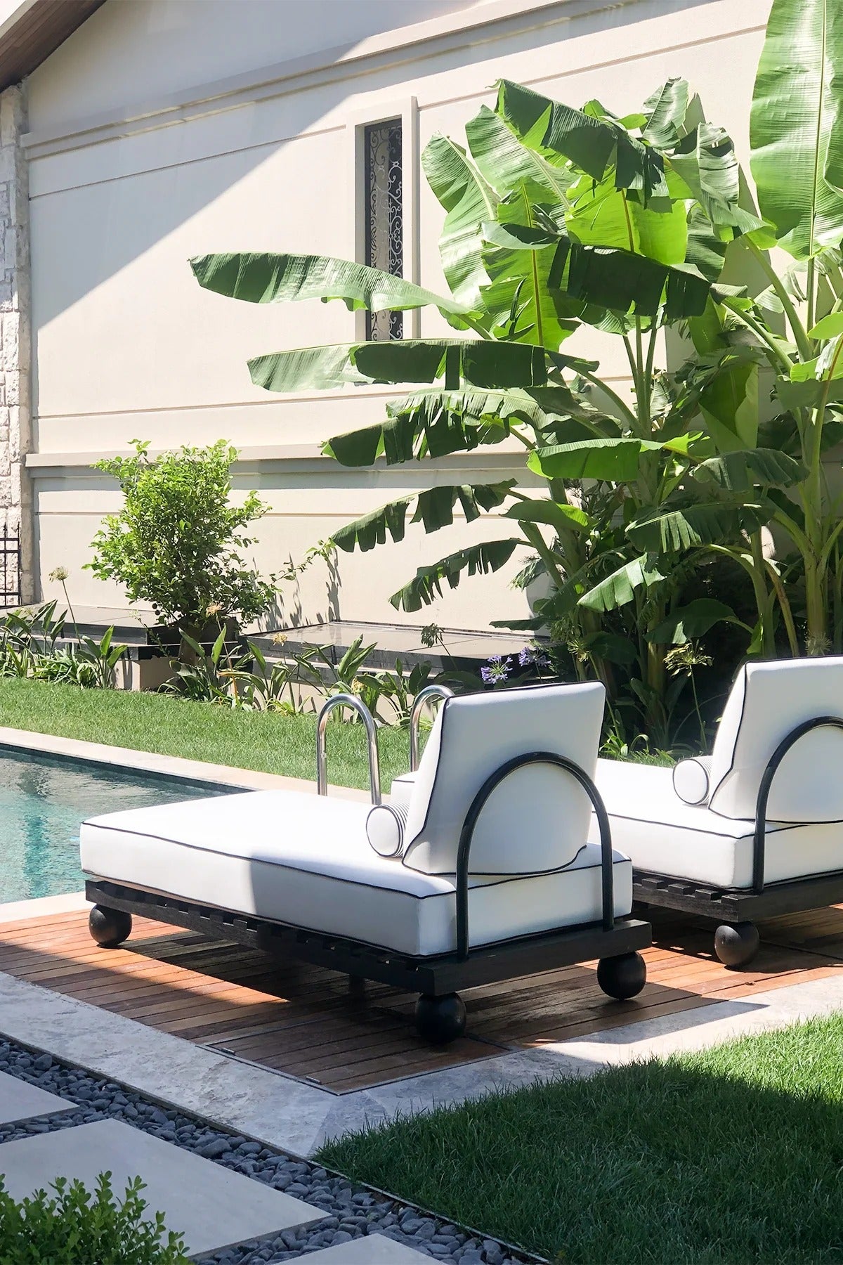 Two white outdoor lounge chairs with black frames on a patio near a pool.