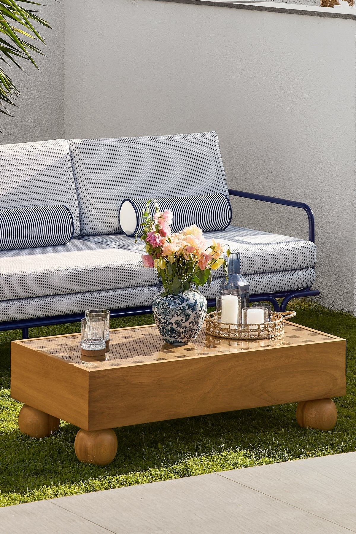 Outdoor sofa and teak coffee table on grass patio furniture.