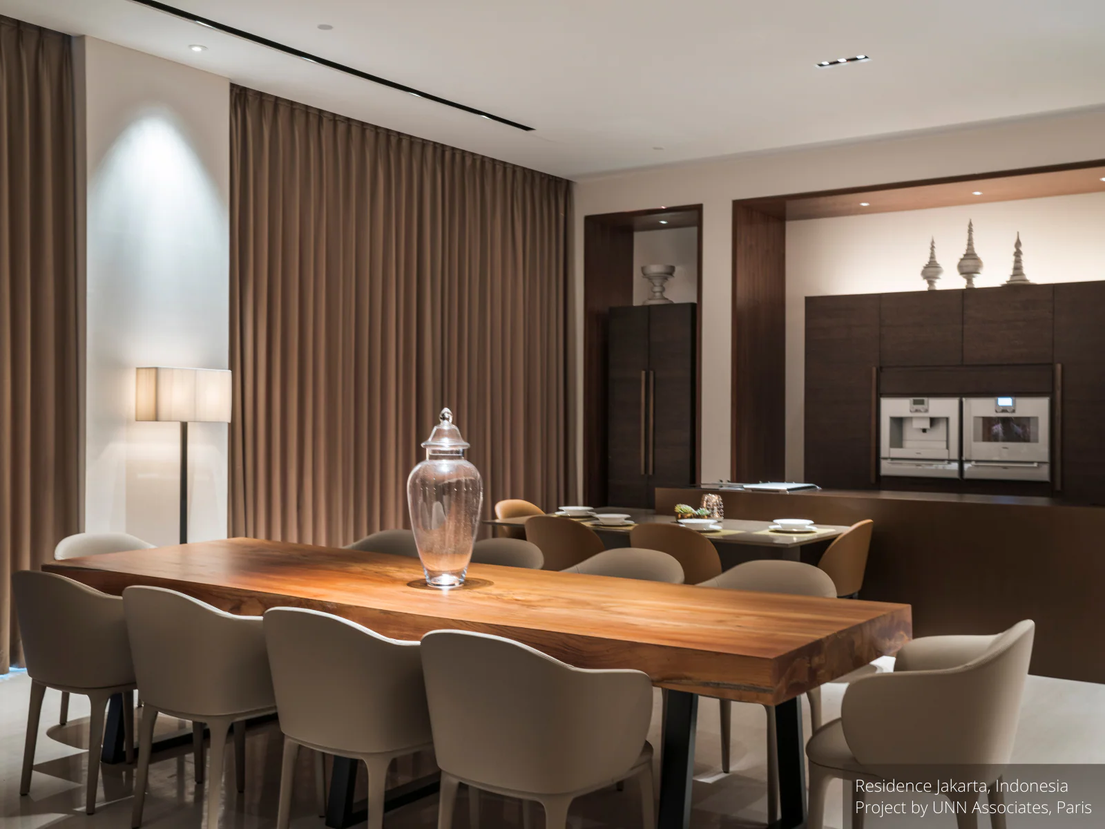 Modern dining room with wooden table and chairs, featuring a kitchen in the background.