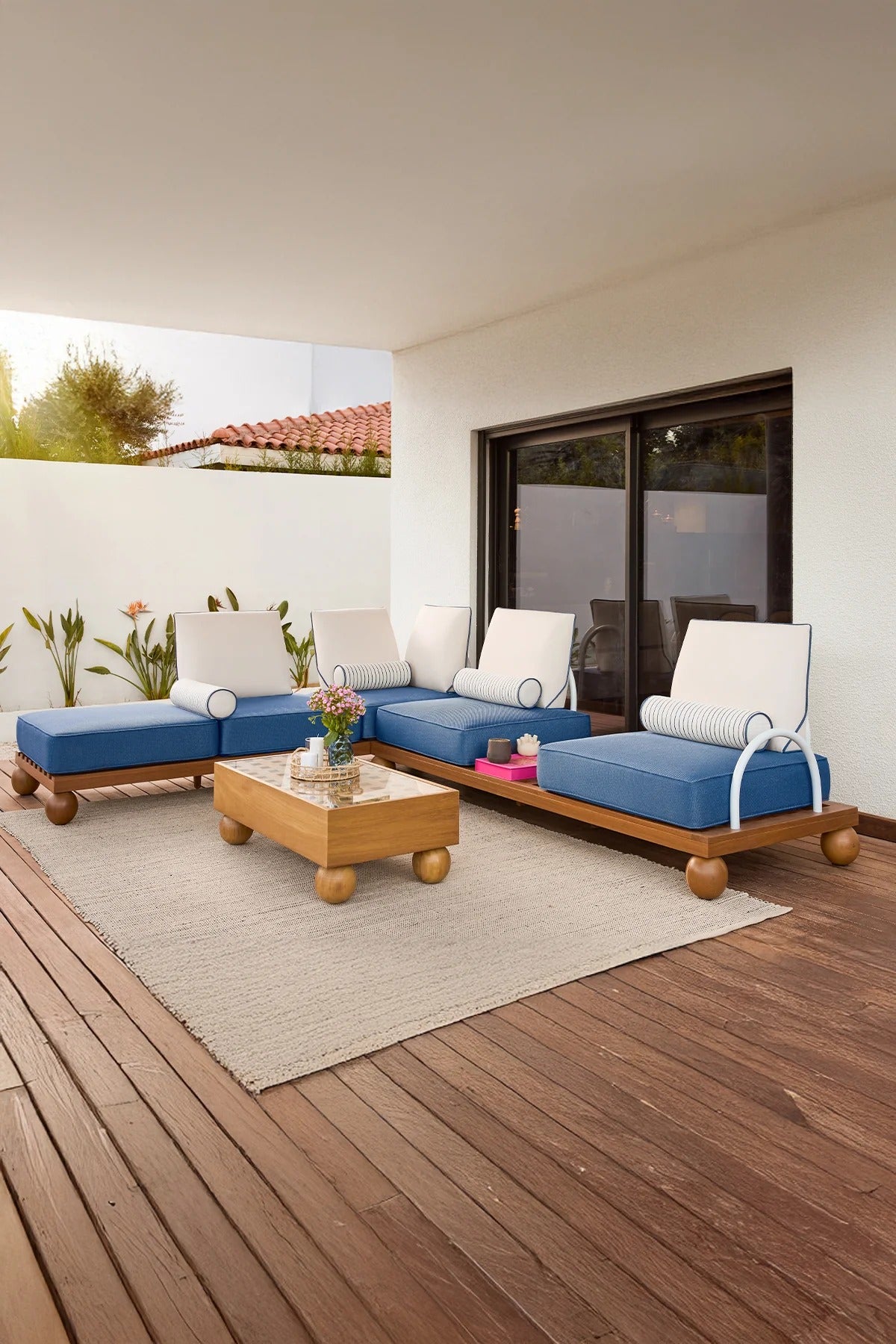 Santa Cruz outdoor corner set made of solid iroko wood with blue cushions, cream backrests, and striped bolster pillows on a natural wooden deck.