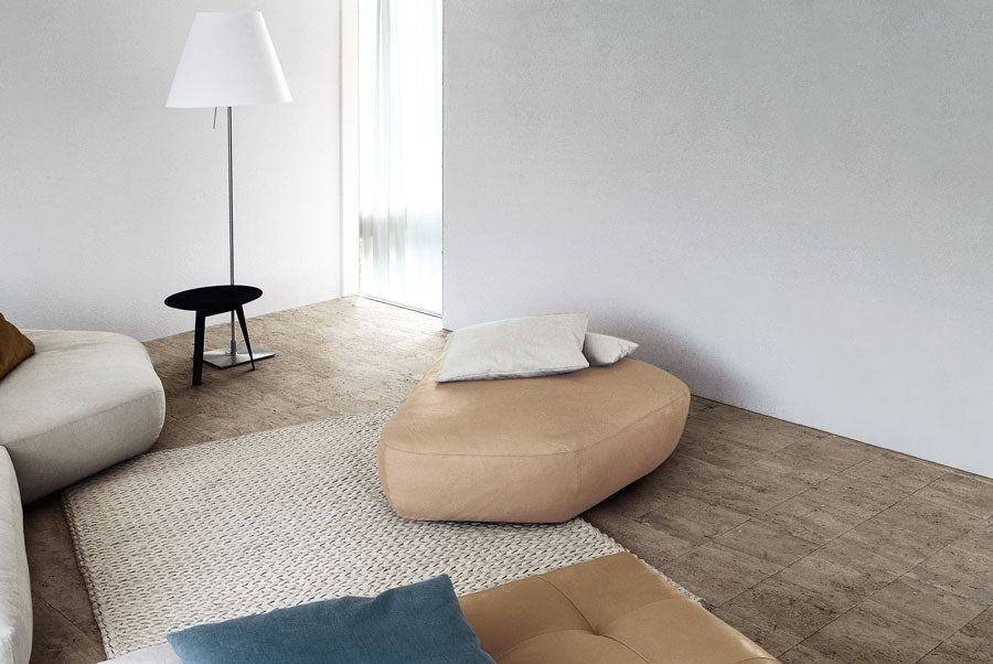 View of modern living room with beige ottoman, white floor lamp, woven rug.