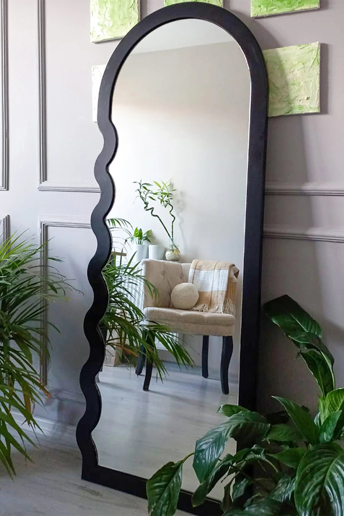 Decorative floor mirror with a black wavy design in a room with plants and a chair.