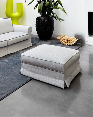 Modern living room with white slipcover sofa, gray ottoman, black cabinet, gray rug, and green decor.