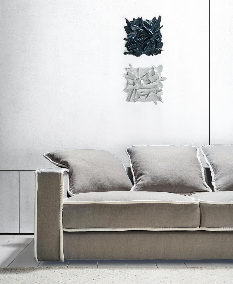  Close-up of a modern gray linen sofa with white piping, featuring decorative wall art. Keywords: sofa, linen, gray, modern furniture, living room, home decor.