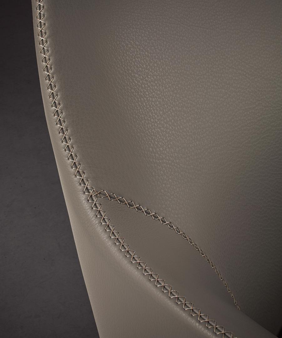  Close-up of the Casamilano Liz chair's gray leather, showcasing meticulous stitching detail. Luxury furniture with modern design elements