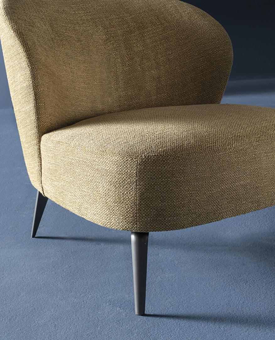 Close-up of the Casamilano Dhora Slim armchair featuring a curved back, textured upholstery, and sleek tapered legs