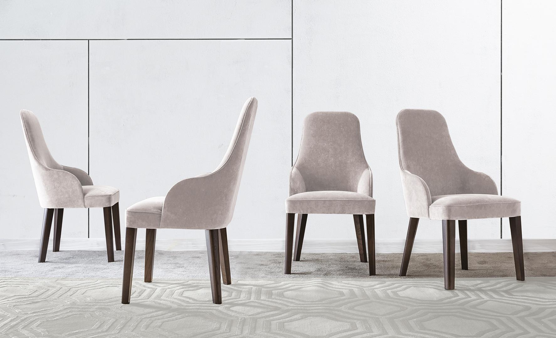 Interior view of Casamilano Diana dining chairs with velvet upholstery and dark wood legs, arranged on a patterned rug in a minimalist setting