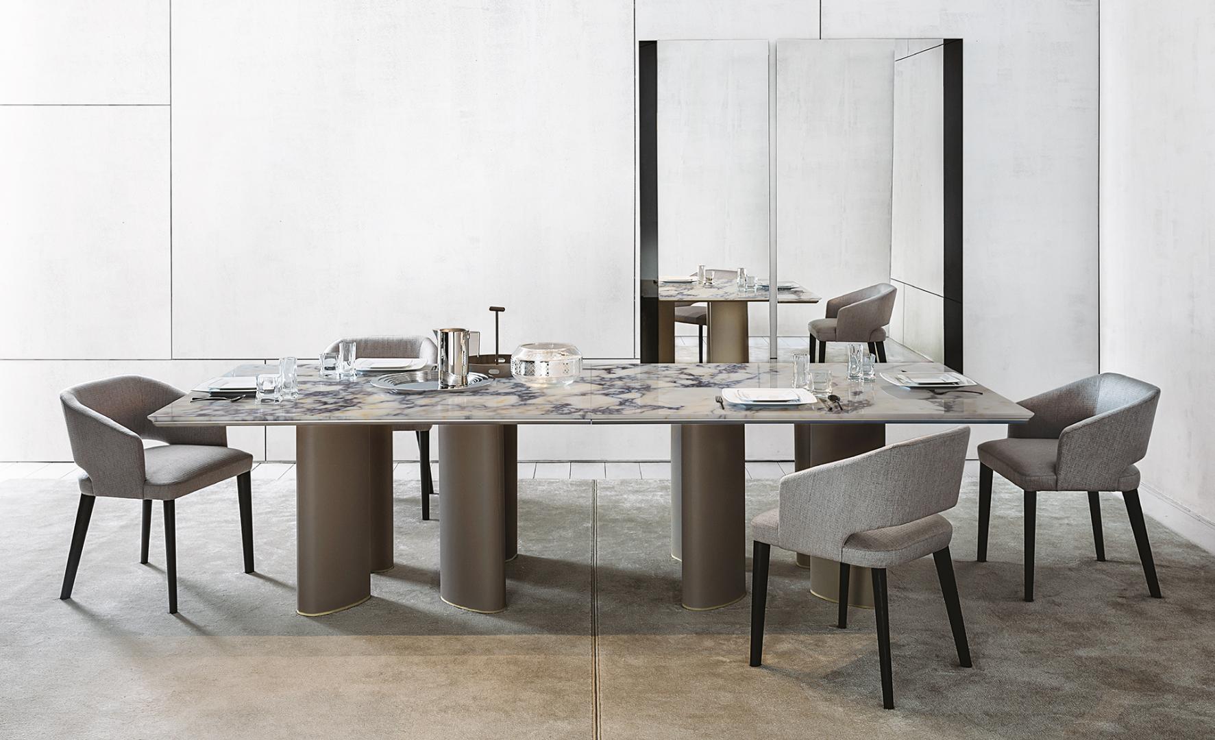 A modern dining room featuring a marble table, dinnerware, and Casamilano Elsa upholstered dining chairs reflected in a large mirror.