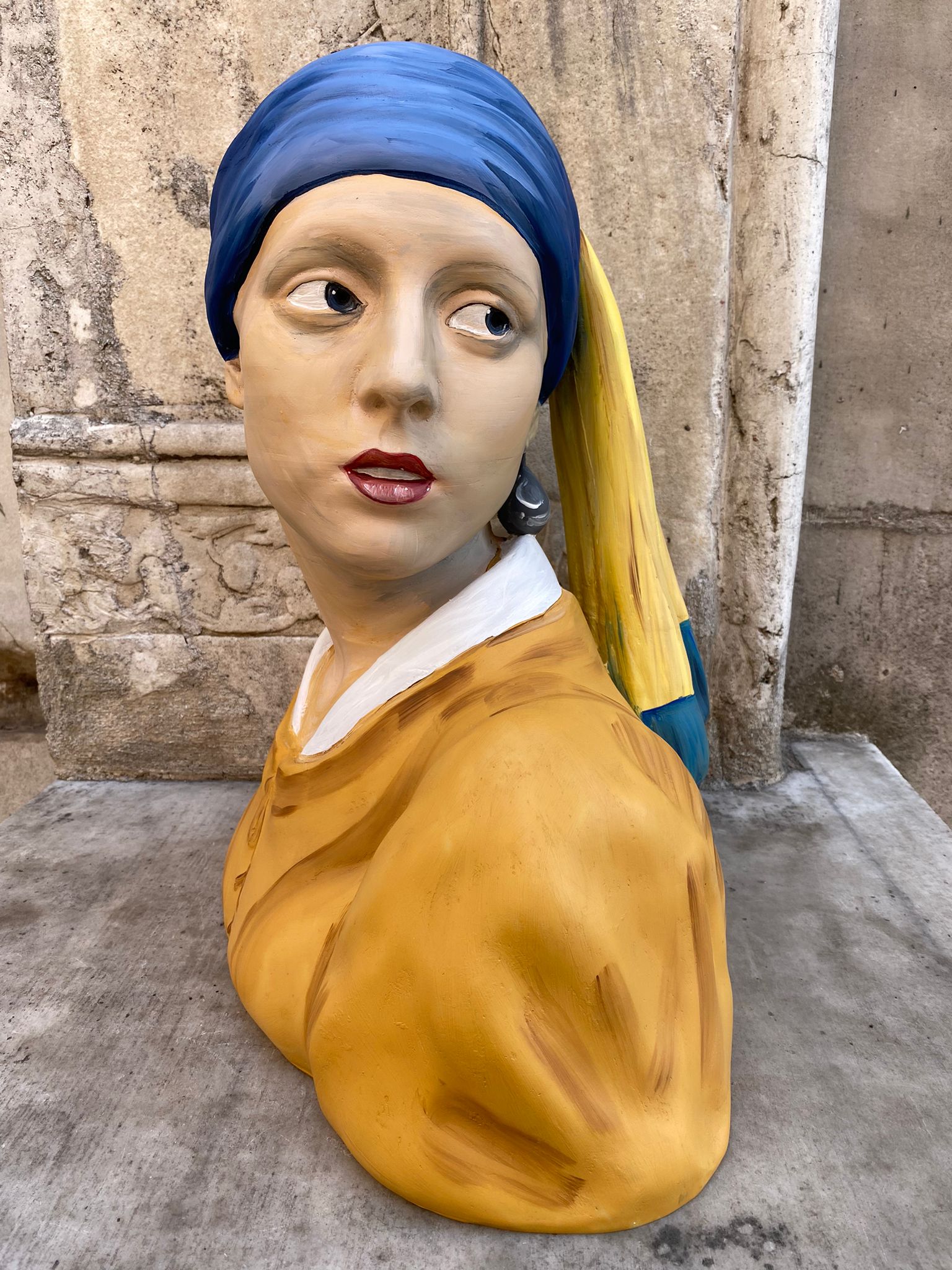 Outdoor sculpture bust of woman with blue and yellow head covering
