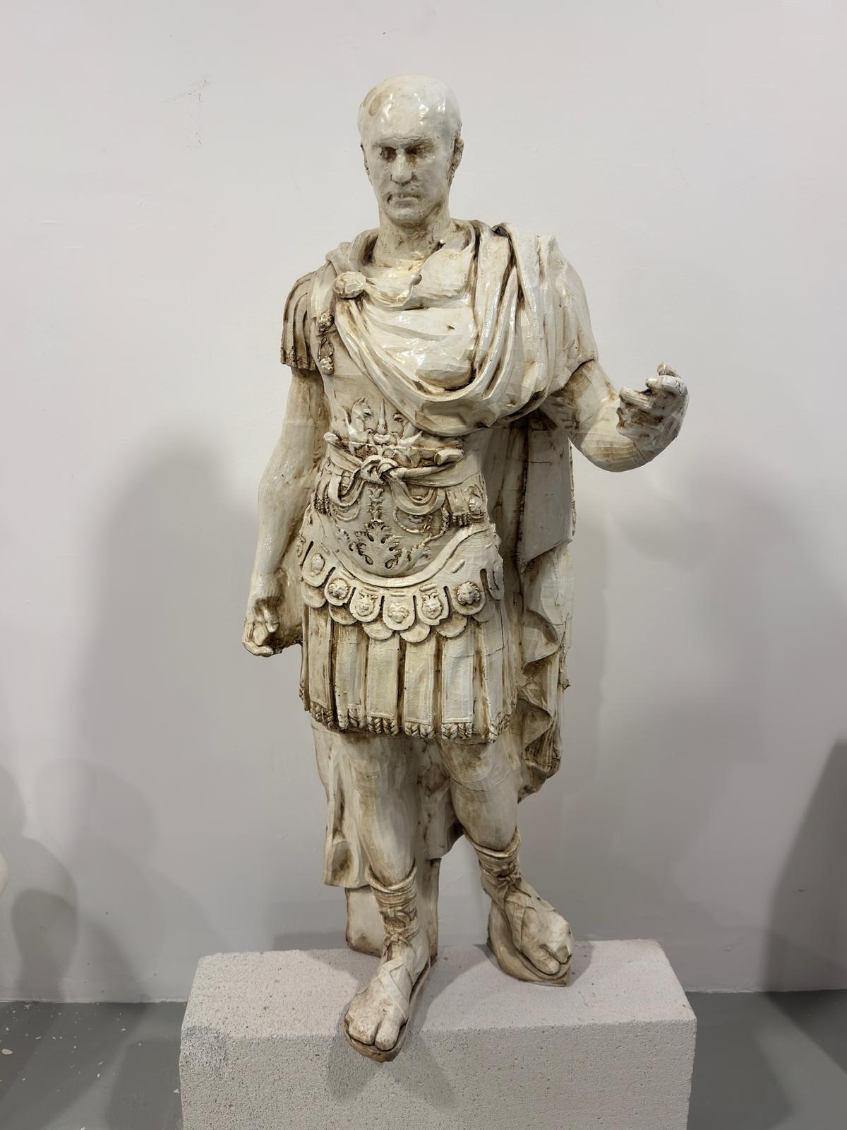 White Roman emperor statue on concrete block against white wall.