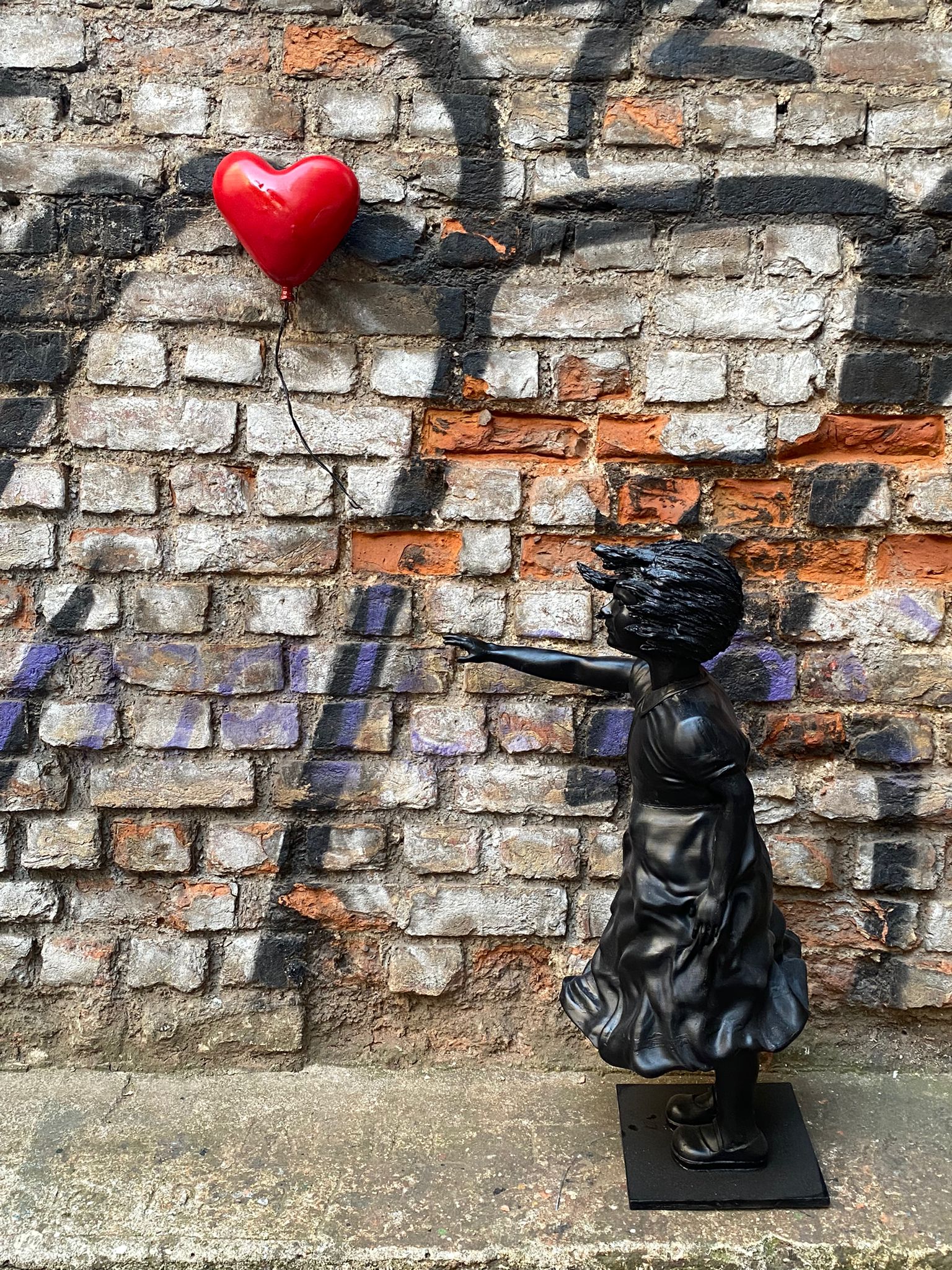 Black girl sculpture with red heart balloon against brick wall