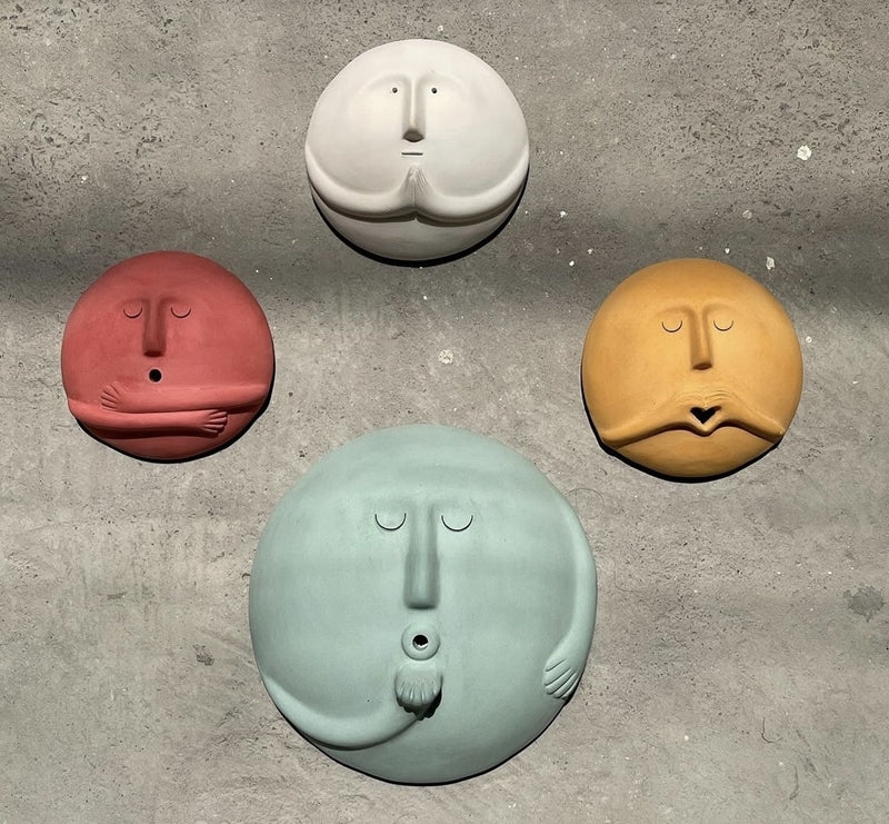 Four colorful round face sculptures mounted on gray wall decor