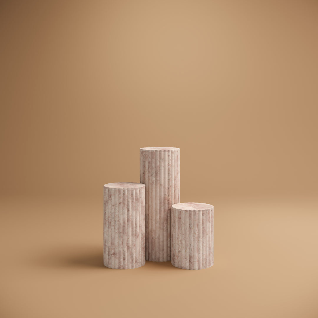 Three Luzione marble product display stands in a minimalist studio setting with a tan background, perfect for showcasing products
