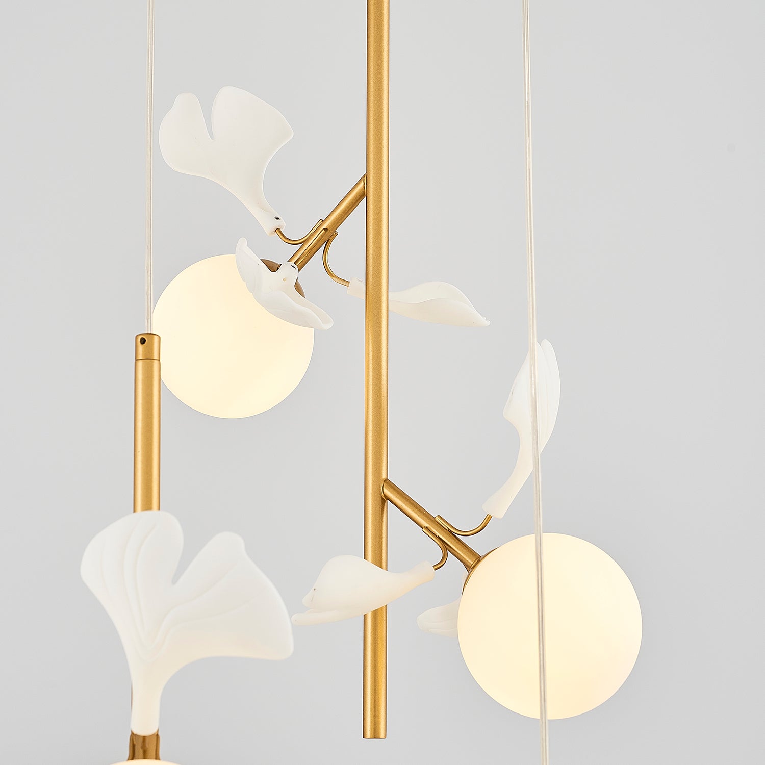 Close up of gold lighting fixture with white glass globes and leaves