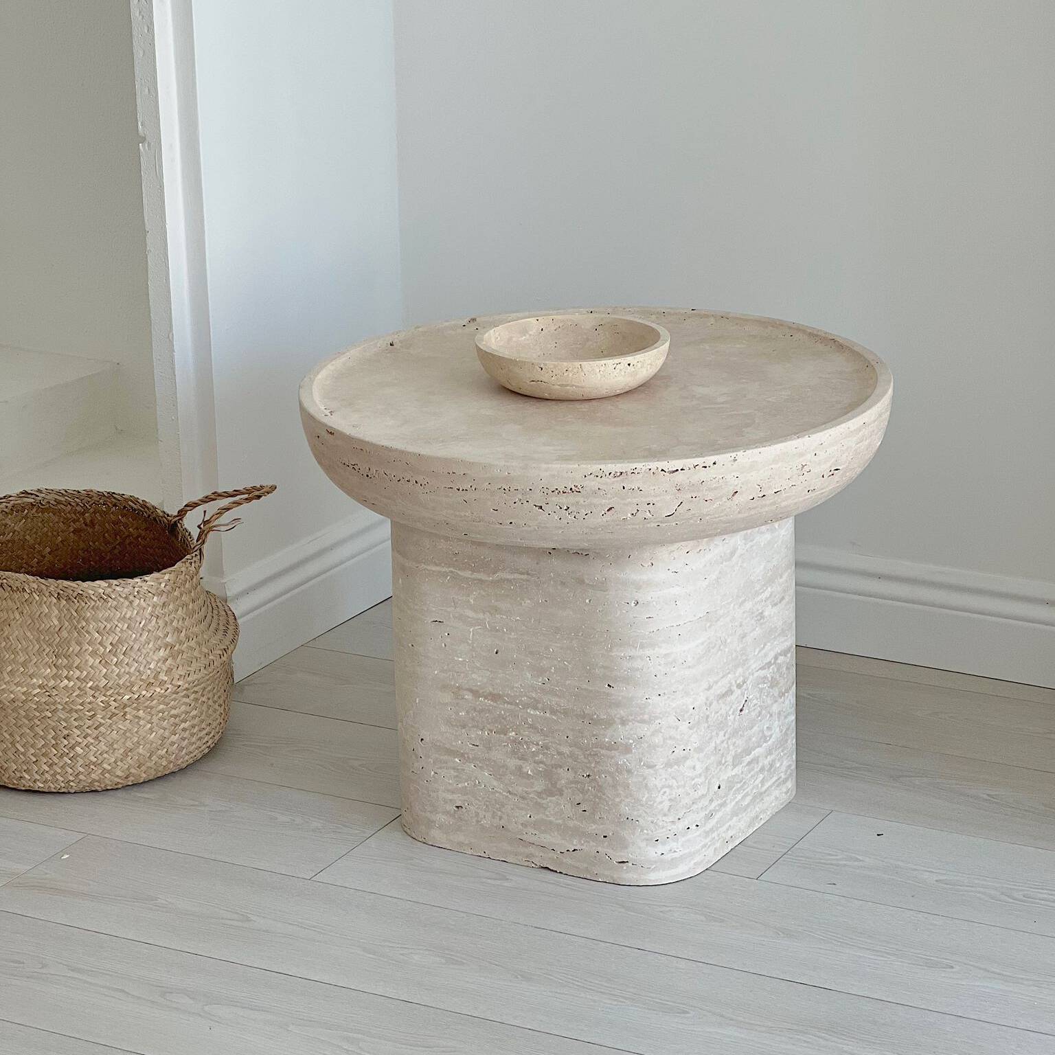 Interior view of Luzione round travertine side table with matching bowl and woven basket, enhancing living room decor with natural stone furniture