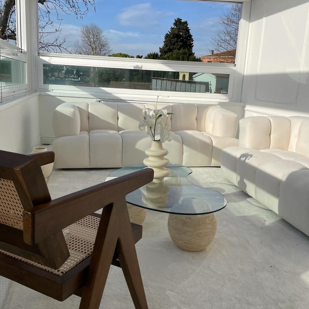 Sunroom featuring Luzione white modular sofa, glass coffee table with sphere base, wooden accent chair, and ample natural light