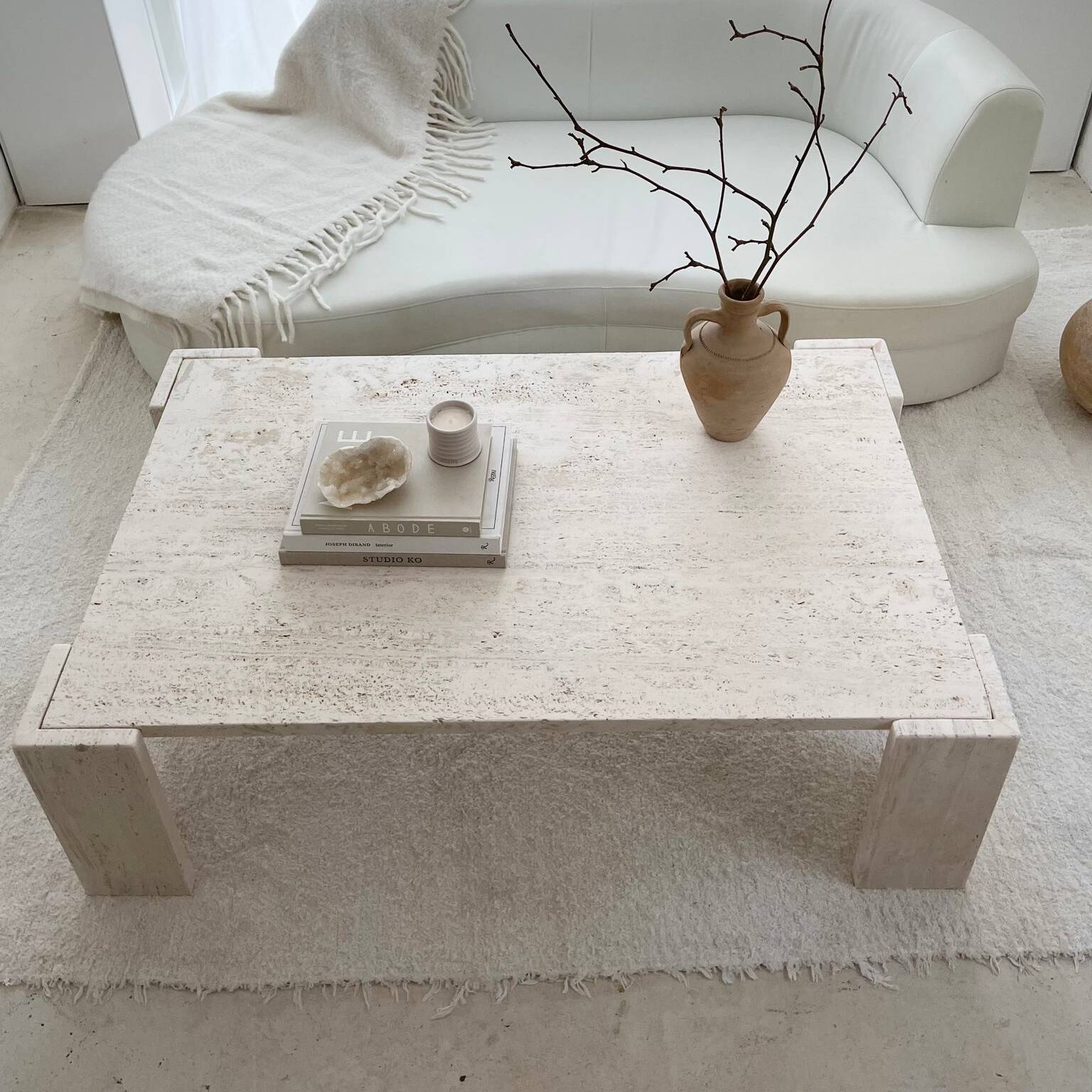 Minimalist living room featuring a Luzione travertine coffee table, curved white sofa, and neutral decor, creating a serene and stylish atmosphere