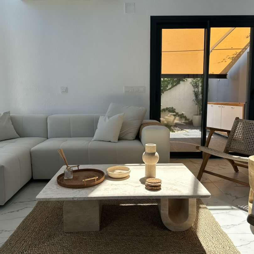 Modern living room featuring a Luzione white sectional sofa, stone coffee table, jute rug, and wicker chair, bathed in natural light
