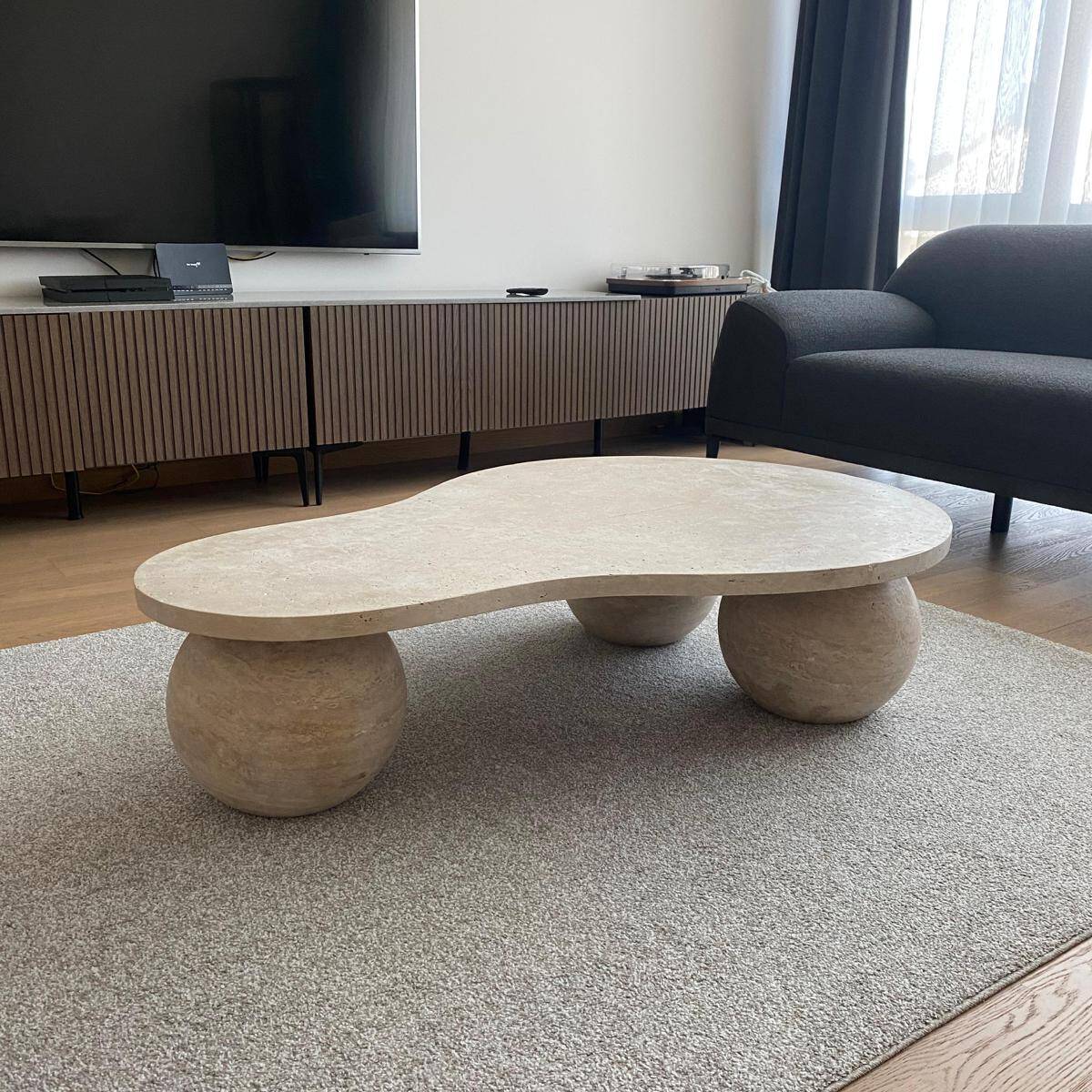Modern living room featuring a Luzione organic-shaped travertine coffee table with spherical legs, a sleek media console, and a contemporary gray sofa