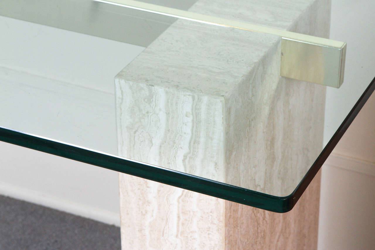 Close-up of Luzione Nishijin table featuring a glass top, travertine base, and elegant brass accents for a modern, sophisticated design