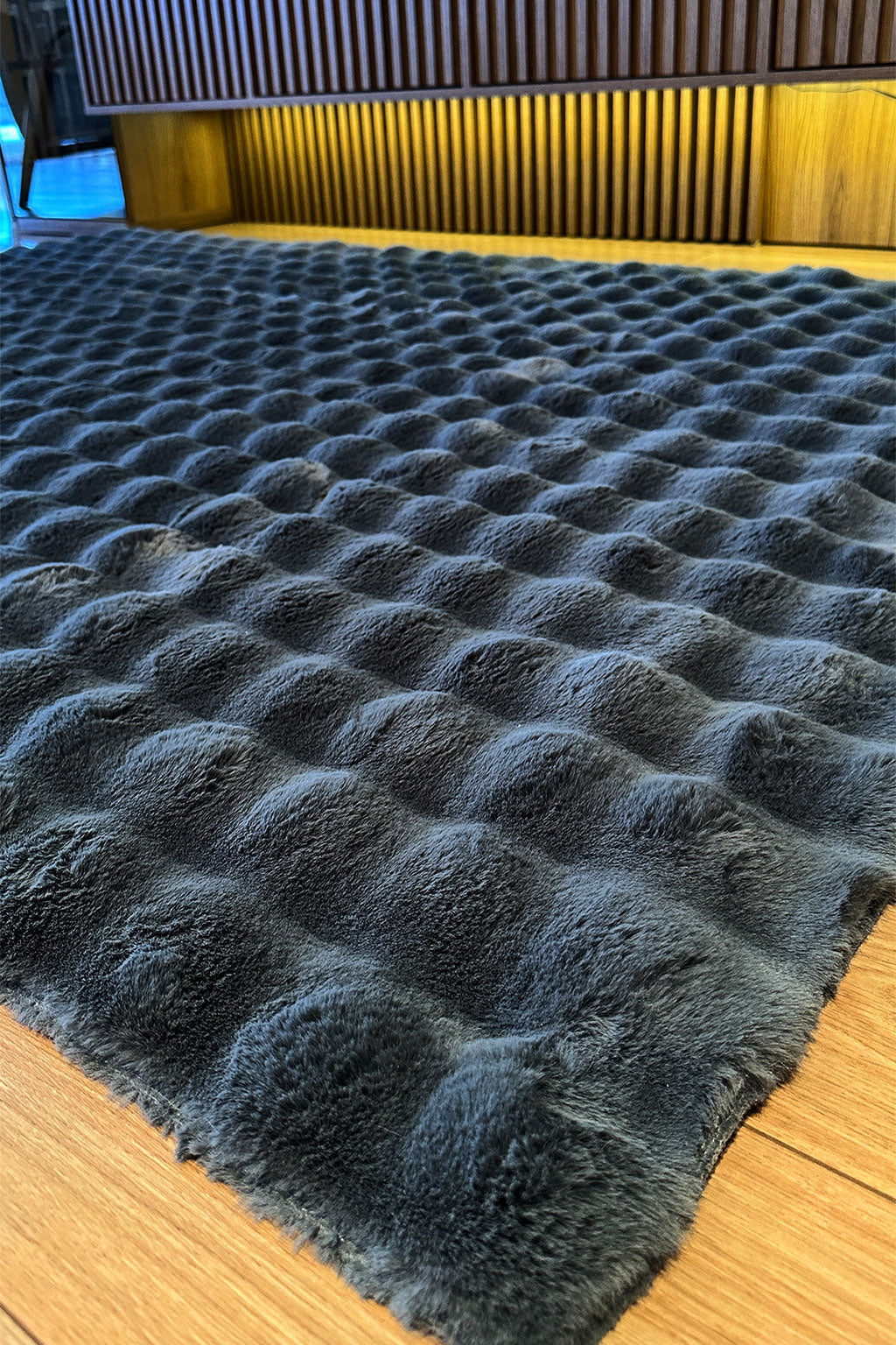 Close up view of dark gray textured faux fur rug on wood floor.