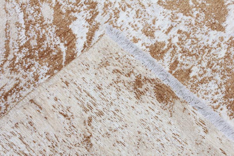 Overhead view of tan and white patterned area rug showing backing and fringe.
