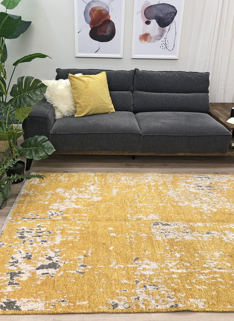 Living room scene with dark gray sofa, yellow abstract rug, and wall art.