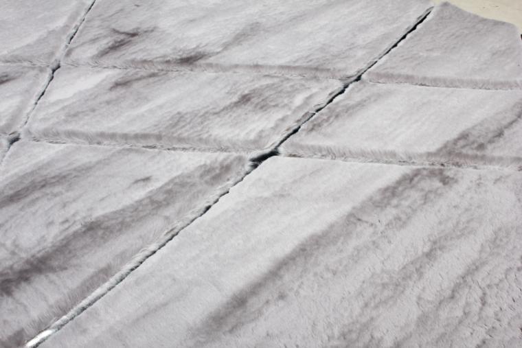 Angled view of Rabbit Fur Rug under a coffee table, highlighting its plushness in a contemporary setting.