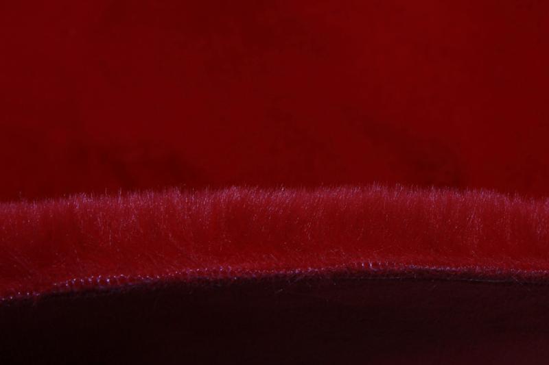 Close up of red faux fur rug edge showing stitching