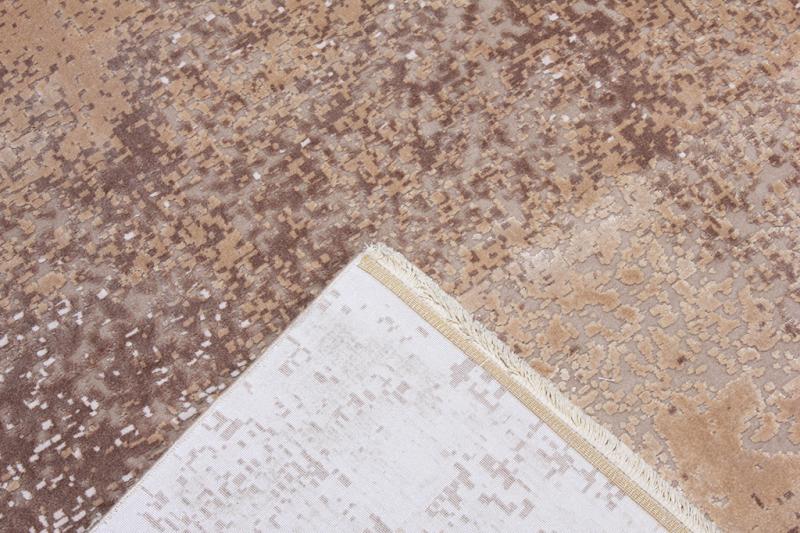Overhead view of beige and brown patterned rug with turned corner showing backing.
