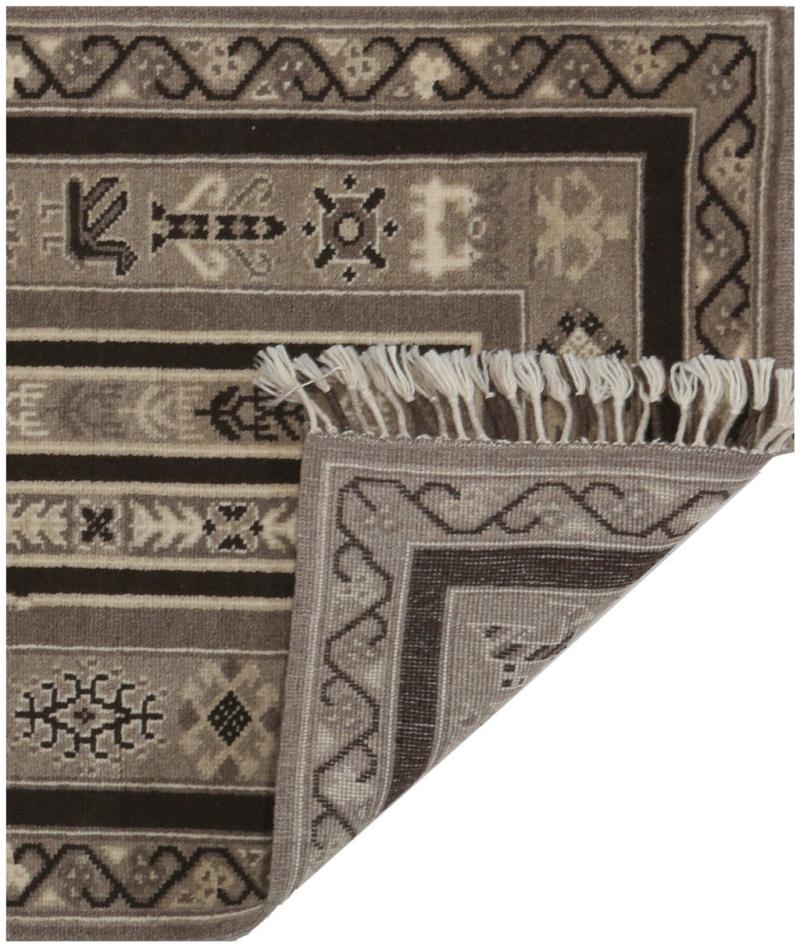 Overhead view of brown patterned rug with corner folded showing fringe.