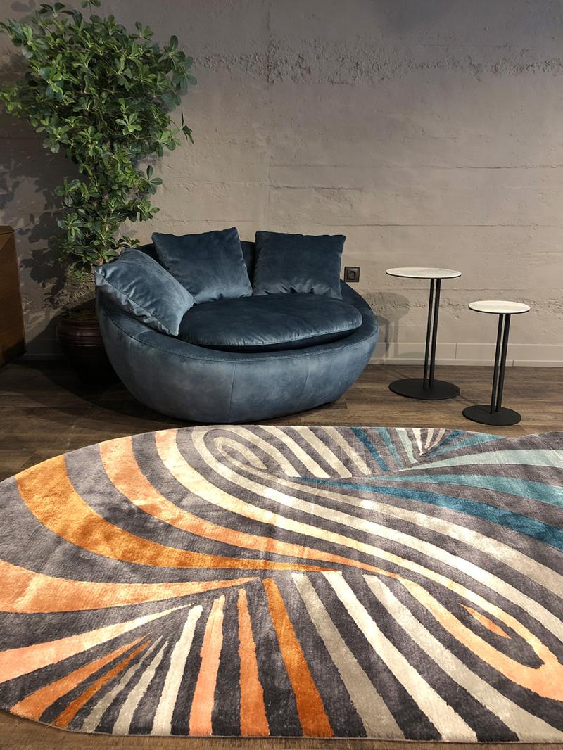 Interior view of blue velvet round sofa, two white side tables, and striped area rug