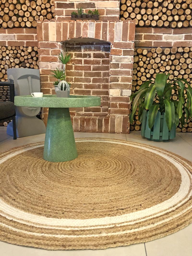 Living room with Luzione 915 Urban jute rug, green pedestal side table, brick fireplace, and firewood. Eco-friendly, rustic interior design