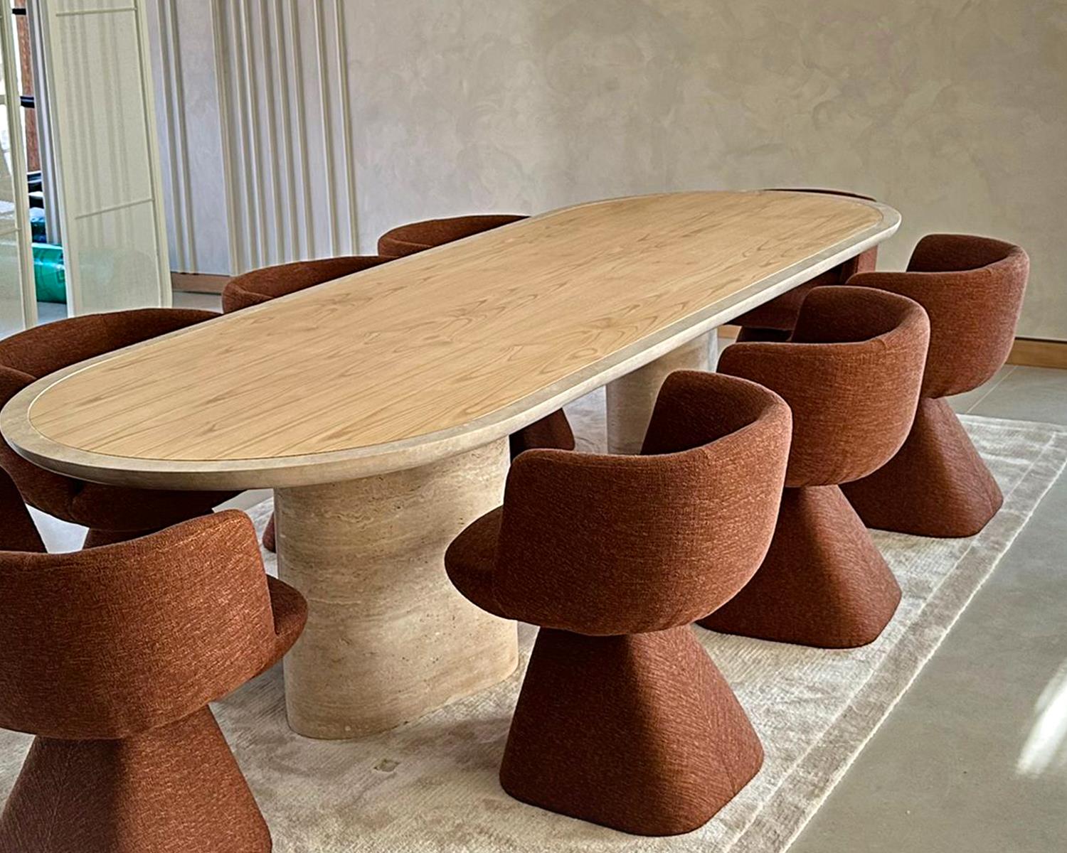 Dining table with wood top and stone base surrounded by brown chairs on rug
