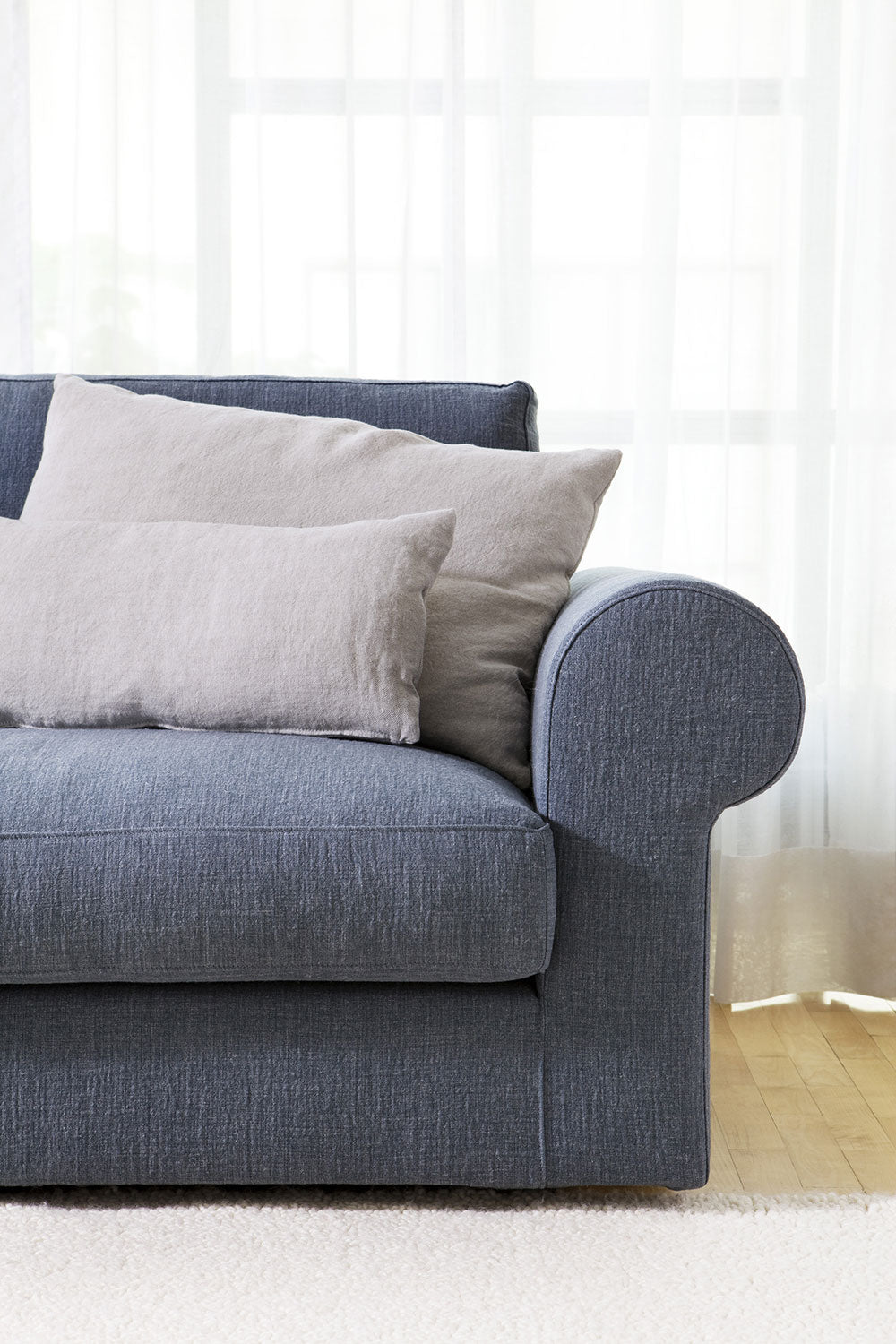 Close up blue fabric sofa with beige pillows, sheer curtains, wood floor