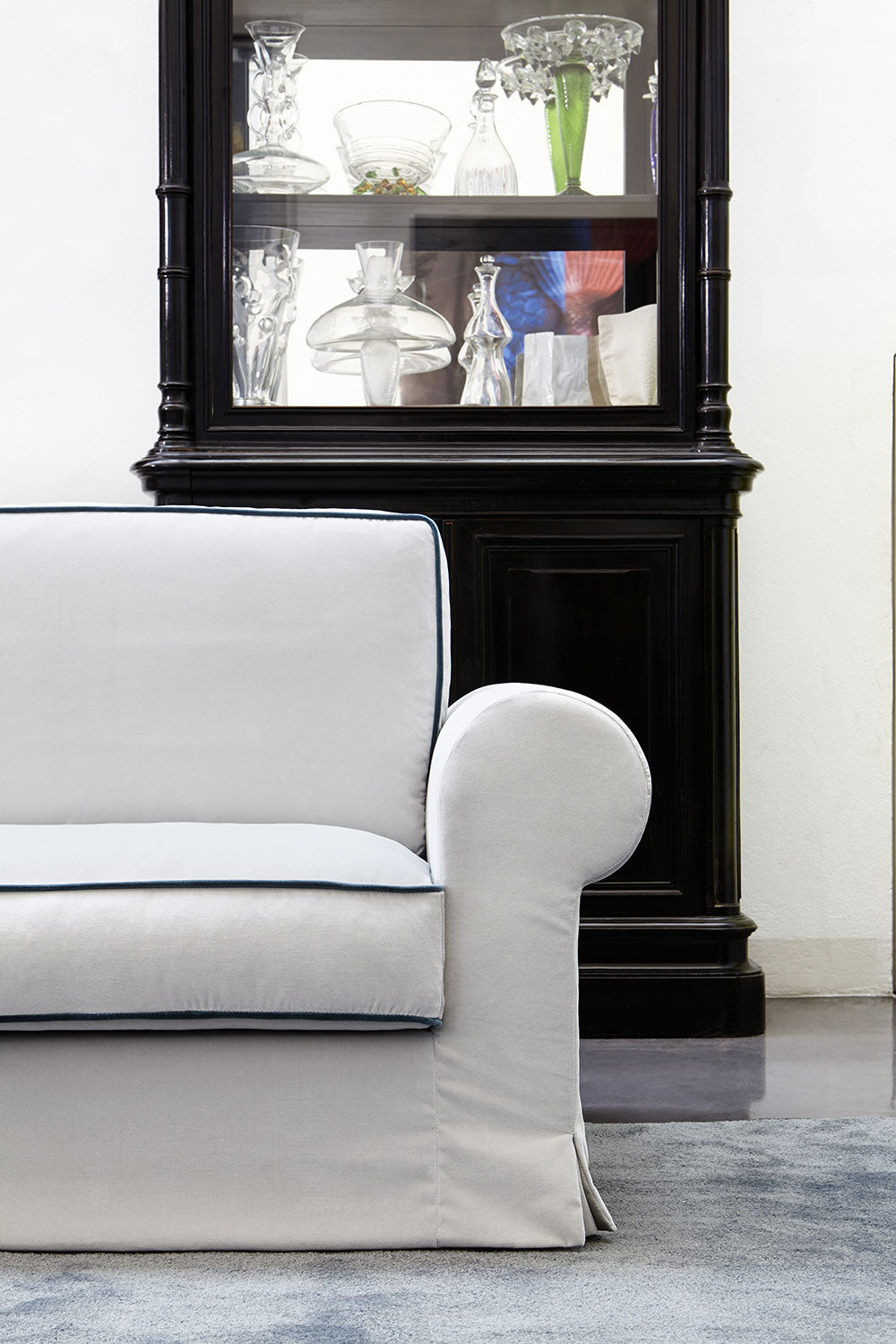 White fabric sofa with skirt and black display cabinet filled with glass objects, furniture.