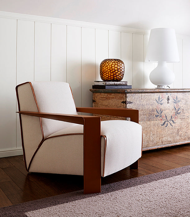 View of upholstered armchair with wood frame next to painted wooden chest.