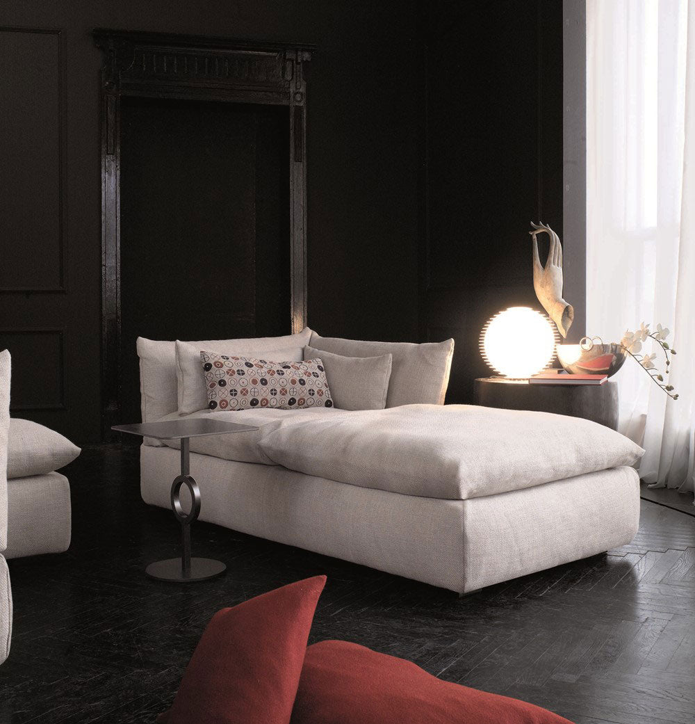 Dark room view with beige chaise lounge sofa, side table, lighting, decor.